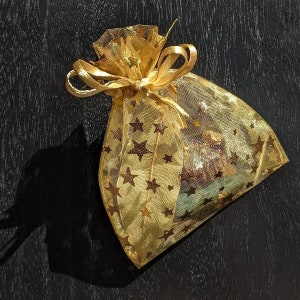May include: A gold mesh gift bag with a gold ribbon and gold stars. The bag is empty.