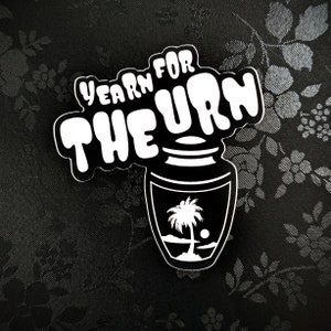 May include: Black and white sticker with the text "Yearn for the Urn" in a wavy font. The sticker features a black and white illustration of a stylized urn with a palm tree inside.