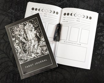 May include: A black and white tarot journal with a black cover featuring a drawing of a woman sitting in a forest. The journal has a moon phase tracker and space for journaling about tarot readings.