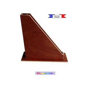Peut inclure: Un porte-revues en bois de forme triangulaire avec une finition brun foncé. Le porte-revues a une petite ouverture en haut pour insérer des magazines. Le texte "ZG-jouets bois- " est imprimé sur le bas du porte-revues.