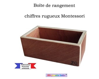 May include: A wooden box with a light brown interior and a dark brown exterior. The box is labeled "ZG" and has the text "ZG-jouets bois-." The box is for storing Montessori rough-textured number blocks. The text "Boîte de rangement chiffres rugueux Montessori" is above the box. A red, white, and blue ribbon with the text "Fabrication Française artisanale" is below the box.