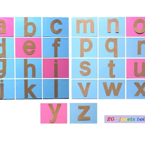 Könnte beinhalten: Ein Satz Alphabet-Buchstaben-Kacheln in Braun auf blauem und rosa Hintergrund. Die Buchstaben sind in alphabetischer Reihenfolge angeordnet. Der Text "ZG - jouets bois -" ist am unteren Rand des Bildes sichtbar.