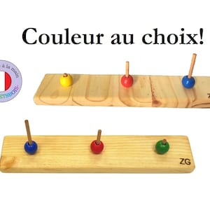 Pode incluir: Duas bases de brinquedo de madeira com pinos e bolas coloridas. As bases são de madeira natural e têm um design simples. As bolas são vermelhas, azuis, amarelas e verdes. O texto "Couleur au choix!" é visível no topo da imagem. O texto "ZG" é visível nas bases.
