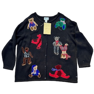 May include: Black cardigan sweater with various colorful teddy bear appliqués. The bears are in different poses and outfits, including a blue and red outfit, a leopard print, and a red scarf. The sweater has a button-up front and a tag.
