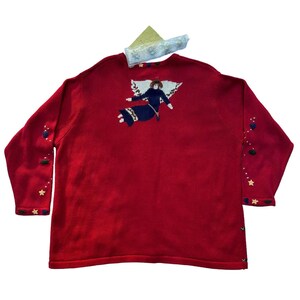 May include: Red knitted sweater with a festive angel design and star accents.