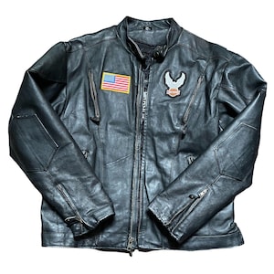 May include: Black leather motorcycle jacket with a zipper closure, multiple pockets, and a small American flag patch. The jacket features a Harley-Davidson emblem on the chest and padded elbow patches.