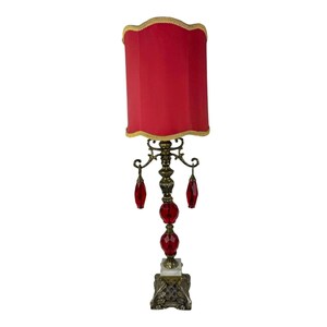 Puede incluir: Una lámpara roja con base dorada y detalles de cristal rojo. La pantalla es roja con ribete dorado.
