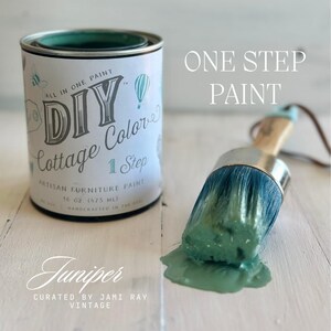 May include: A 16 ounce (475 ml) jar of teal green "DIY Cottage Colors" one-step artisan furniture paint. The jar has a white label with the text "All in One Paint" and "DIY Cottage Colors" in a whimsical font. The paint is labeled "Juniper" and is curated by Jami Ray Vintage. A paintbrush with teal green paint on it is in the background.