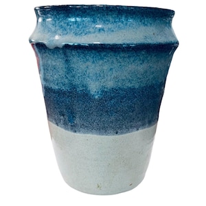Può includere: Un vaso in ceramica fatto a mano con una sfumatura di colori. La parte superiore è blu scuro, che sfuma in blu più chiari e termina con una base bianca. Il vaso ha un bordo leggermente svasato e una superficie strutturata.