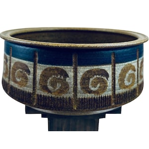 May include: A brown ceramic planter with a blue and white geometric design. The planter has a wide, round base and a slightly flared rim.