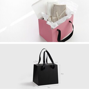 May include: Two gift bags, one pink and one black. The pink bag is open and has white tissue paper inside. The black bag has black ribbon handles and is 16 cm wide, 14 cm tall, and 12 cm deep.