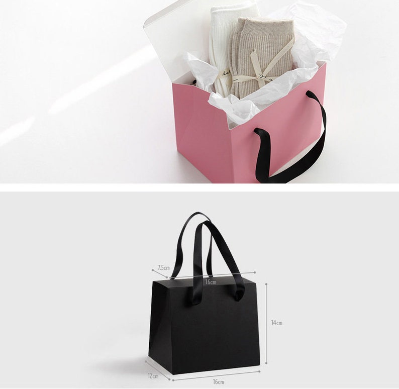 May include: Two gift bags, one pink and one black. The pink bag is open and has white tissue paper inside. The black bag has black ribbon handles and is 16 cm wide, 14 cm tall, and 12 cm deep.