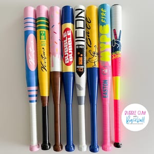 May include: A collection of eight baseball bats with colorful designs. The bats feature various patterns, including stripes, sprinkles, and text. One bat has a banana graphic. The bats are approximately 30 inches long.