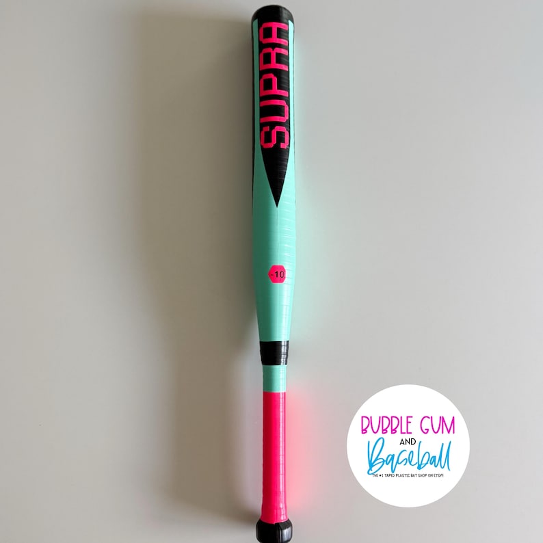May include: A mint green and pink baseball bat with the word "SUPRA" in pink lettering. The bat has a black handle and a pink grip. The number "10" is printed in pink. The bat is on a white background.