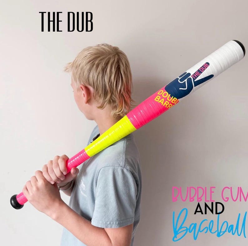 May include: A baseball bat featuring a gradient design that transitions from a bright pink handle to a neon yellow midsection and a white barrel. The barrel displays a dark blue hand graphic, the text THE DUB, and the words DOUBLE BARREL.
