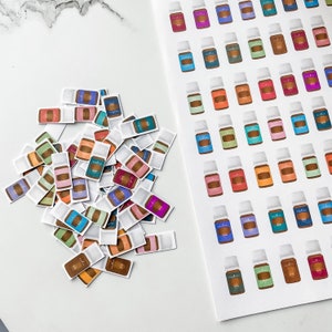 以下が含まれることがあります： さまざまな色のラベルとボトルの色合いを持つ、カラフルなエッセンシャルオイルボトルのステッカー。いくつかのステッカーは散らばっており、他のステッカーは白いシートに配置されています。ラベルには「Young Living」の文字が表示されています。