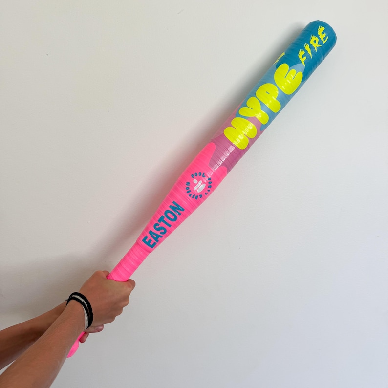 May include: A baseball bat with a blue and pink gradient design. The bat has the text "Hype Fire" in yellow and "Easton" in pink. The bat is held by a person.