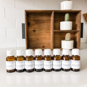 May include: Ten small brown glass bottles with white lids and white labels. The labels have black text that reads "Sleep diffuser blend", "Wellness diffuser blend", "Calming diffuser blend", "Seasonal diffuser blend", "Cozy Home diffuser blend", "Clean Home diffuser blend", "Energy diffuser blend", and "Breathe diffuser blend".