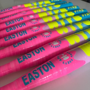 May include: A row of baseball bats in vibrant pink and blue. The bats feature the word "EASTON" in teal, and the words "FIRE" and "PARTY" in yellow and white. The bats are arranged in a row.