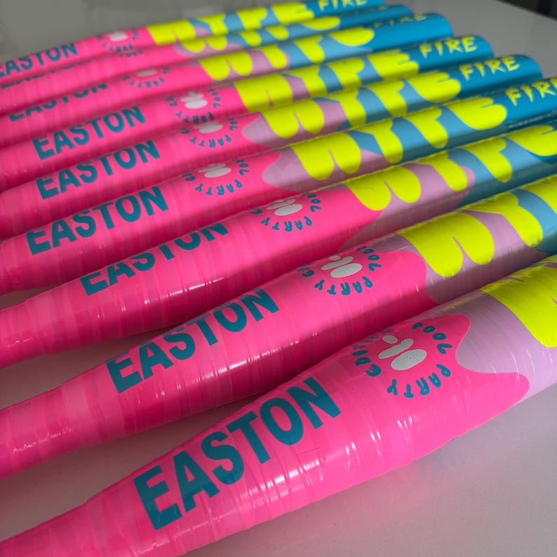 May include: A row of baseball bats in vibrant pink and blue. The bats feature the word "EASTON" in teal, and the words "FIRE" and "PARTY" in yellow and white. The bats are arranged in a row.