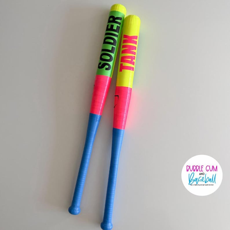 May include: Two plastic baseball bats featuring a color-blocked design with neon yellow, bright pink, and light blue sections. One bat has the word SOLDIER printed in black, and the other has the word TANK printed in black. A circular logo reads BUBBLE GUM AND BASEBALL.
