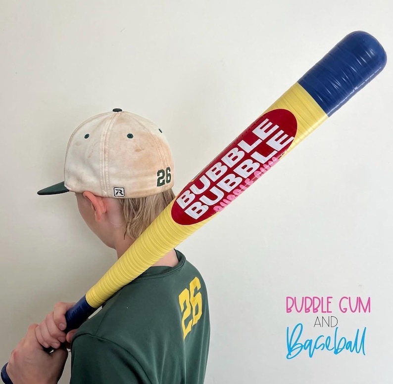 May include: A yellow baseball bat with blue ends and a red oval logo featuring the white text BUBBLE BUBBLE, paired with a cream-colored baseball cap with a green brim and the number 26, and a green shirt with the yellow number 26 on the back.