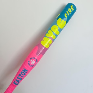 Puede incluir: Un bate de b&eacute;isbol inflable con un esquema de colores vibrantes en rosa brillante, azul y amarillo. El texto HYPE FIRE est&aacute; impreso en letras amarillas grandes, mientras que la palabra EASTON y la frase POOL PARTY EDITION aparecen en azul.