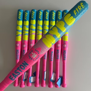 May include: A selection of baseball bats in vibrant pink and blue. The bats feature the words "HYPE FIRE" in yellow and blue, and "EASTON" in teal. Each bat has a pink grip and a blue tag.