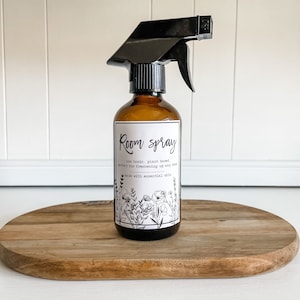 May include: A brown glass bottle with a black spray nozzle. The bottle has a white label with the text "Room spray" and the words "non toxic, plant based, perfect for freshening up any room, made with essential oils".