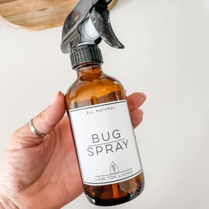 May include: A brown glass bottle with a black spray nozzle and a white label that reads "ALL NATURAL BUG SPRAY LOW TOX LIVING".