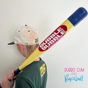 May include: A yellow and blue baseball bat with the text "BUBBLE BUBBLE" in red and white. The bat is held over the shoulder of a person wearing a green shirt and a baseball cap with the number 26.