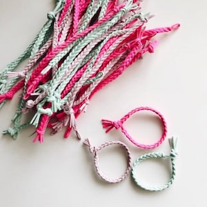 May include: A pile of pink and green braided bracelets. The bracelets are made of a soft, flexible material and are tied together in a knot.
