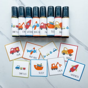 May include: Ten small glass bottles with colorful labels featuring various vehicles and the words "Sniffle", "Calm", "Wellbeing", "Bug Bite", "Owie", "Sleep", "Brave", and "Wellness".  The bottles are arranged in a row on a white marble surface.  Below the bottles are ten small cards with matching vehicle illustrations and the same words as the bottles.