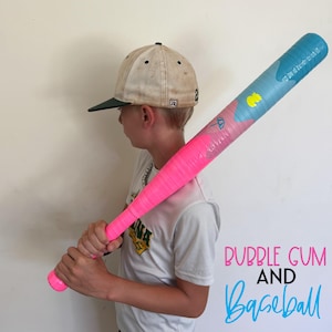 May include: A pink and blue baseball bat with the text "Bubble Gum and Baseball". The bat is held by a person wearing a baseball cap and a white t-shirt. The bat has a pink handle and a blue top.