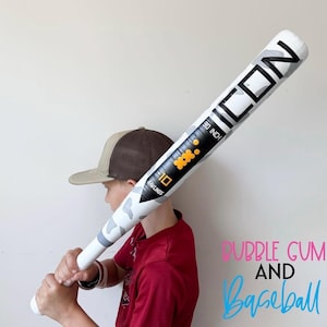 May include: A white and gray camouflage baseball bat with the word "ICON" printed on it. The bat is 30 inches long and has the number "10" printed on it. The bat is held by a person wearing a red shirt and a baseball cap.