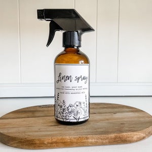 May include: A brown glass bottle with a black spray nozzle and a white label that reads "Linen spray, non toxic, plant based, perfect for freshening up your bedding, made with essential oils". The label has a black and white floral design.