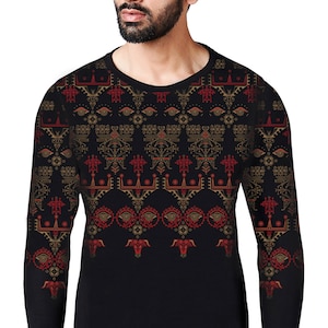 Puede incluir: Camiseta negra de manga larga con un patrón geométrico en dorado y rojo. El patrón presenta ojos estilizados, formas geométricas y cabezas de toro.