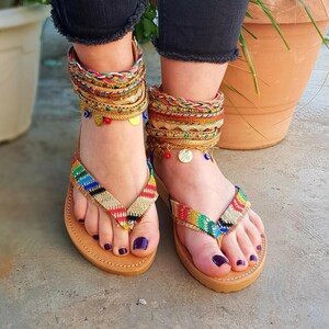May include: A pair of colourful sandals with leather straps and beaded embellishments. The sandals have a brown leather sole and are being worn.