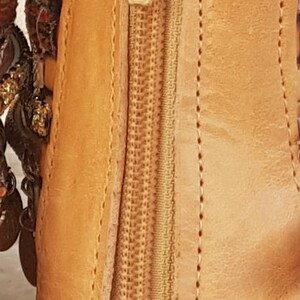 May include: Tan leather ankle boot with a zip up the back. The zip has a gold pull tab with the word "FIM" on it.