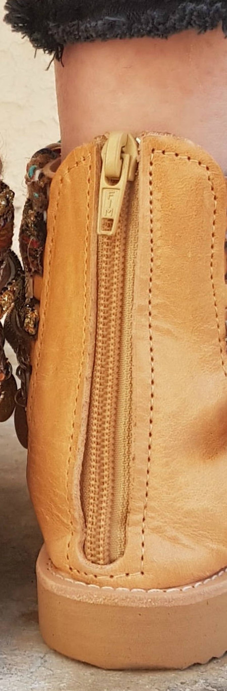 May include: Tan leather ankle boot with a zip up the back. The zip has a gold pull tab with the word "FIM" on it.