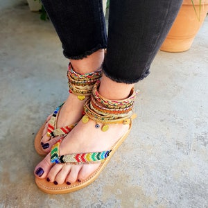 May include: A pair of brown leather sandals with colourful woven straps and gold accents. The sandals have a simple design and are perfect for summer.