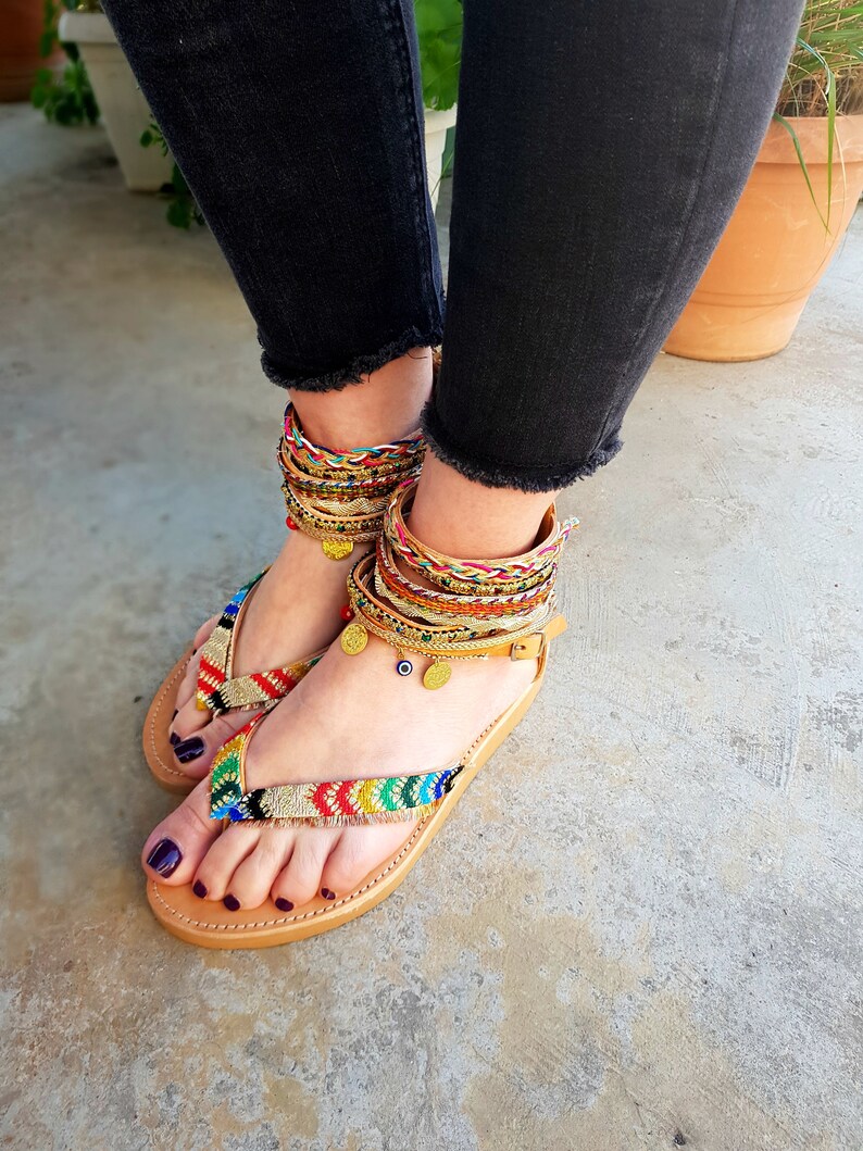 May include: A pair of brown leather sandals with colourful woven straps and gold accents. The sandals have a simple design and are perfect for summer.