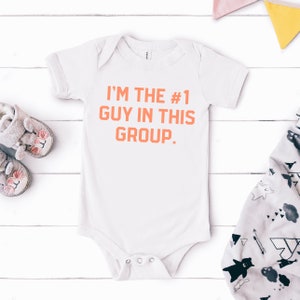 May include: White baby onesie with the text "I'M THE #1 GUY IN THIS GROUP." printed in orange.