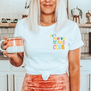 May include: White t-shirt with the text "ANTI POOPOO HEADS CLUB" in colorful letters.