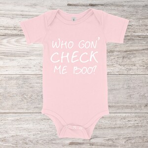 Può includere: Body rosa per neonato con testo bianco che dice "Who gon' check me boo?"