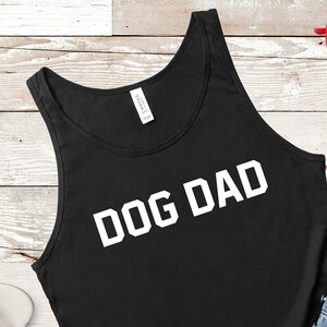Puede incluir: Camiseta de tirantes negra con texto blanco que dice "DOG DAD".