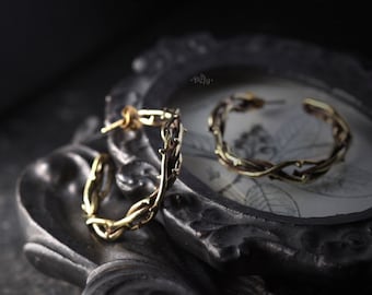May include: A pair of gold hoop earrings with a thorny vine design. The earrings are on a black background.