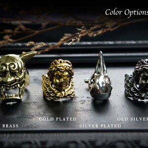 May include: Four rings with different finishes: brass, gold plated, silver plated, and old silver plated. Each ring features a unique design, including a demon face, a winged figure, a bird skull, and a lion head.