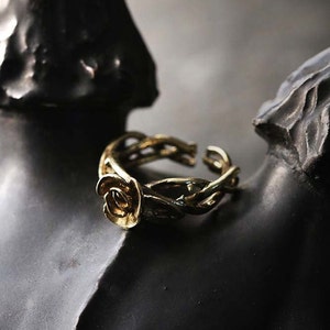 May include: A gold-toned ring with a rose design. The ring is made of twisted metal that resembles vines.