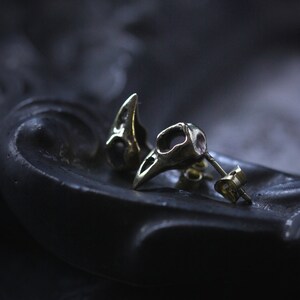 May include: A pair of silver skull-shaped earrings with a detailed design. The earrings are on a black surface.